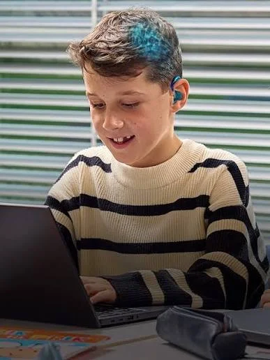 Enfant appareillé avec un appareil auditif Oticon Play, concentré sur son ordinateur en classe